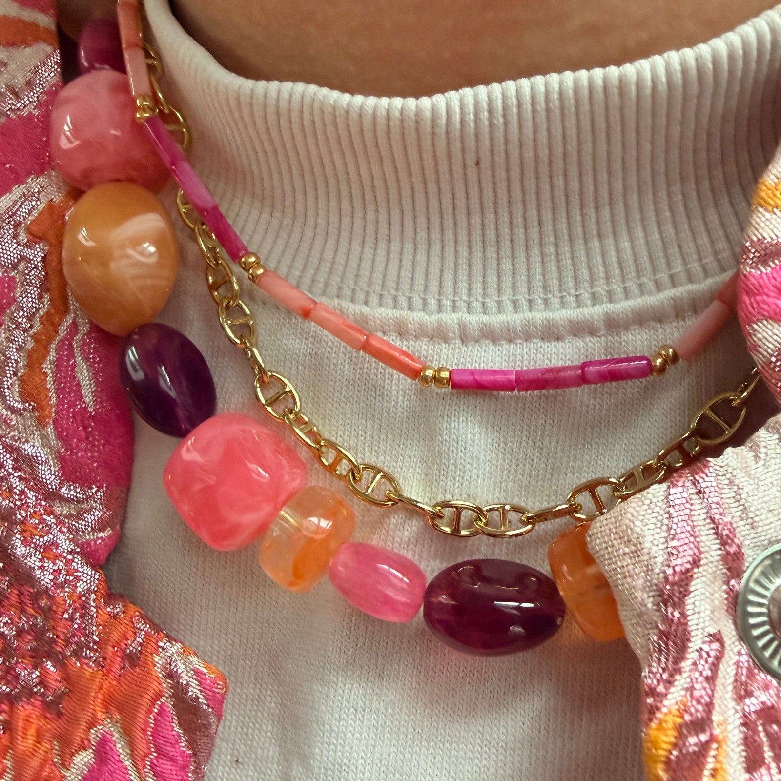 Drie lagen handgemaakte kettingen met diverse kralen in warme tinten zoals fuchsia roze, oranje en dieppaars, gecombineerd met een gouden chain.